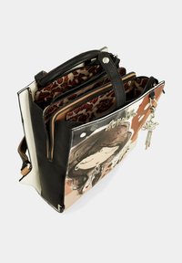 Sac à main en simili cuir noir et blanc avec plusieurs compartiments, présentant une illustration fantaisiste d'un côté et un charm sur une fermeture éclair.