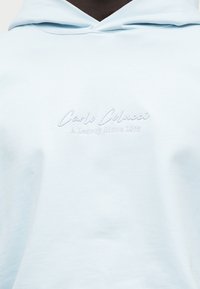 Φούτερ ανοιχτού γαλάζιου χρώματος με διακριτικό κεντημένο κείμενο "Carlo Colucci A Legacy Since 1978" στο στήθος.