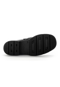 Suela de zapato de goma negra con una superficie texturizada, que presenta un diseño segmentado y un nombre de marca en relieve. Perfil plano con ranuras horizontales.