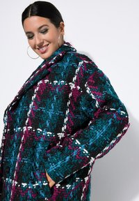 Geruite wollen jas met teal, zwart en magenta, met een gemêleerd afwerking, grote kraag en zijzakken. Dubbele knoopsluiting zichtbaar.