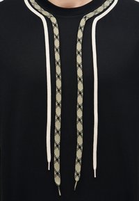 Μαύρο πουκάμισο με δύο λευκές παράλληλες ρίγες και δύο μαύρα μπεζ κορδόνια με σχέδια που κρέμονται μπροστά.