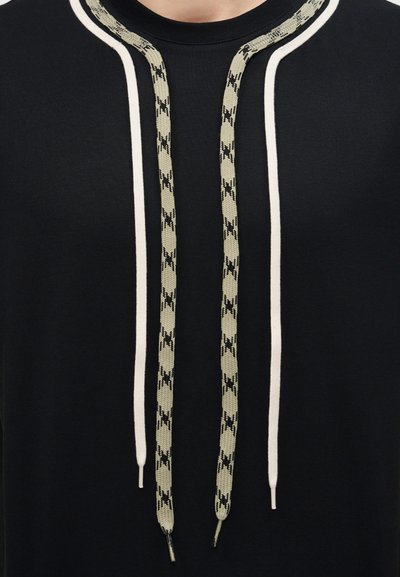 Μαύρο πουκάμισο με δύο λευκές παράλληλες ρίγες και δύο μαύρα μπεζ κορδόνια με σχέδια που κρέμονται μπροστά.