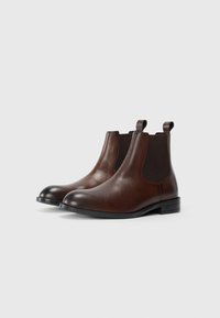 Brown leather Chelsea boots with elastic side panels, rounded toe, and looped heel tabs. Smooth texture and classic design.