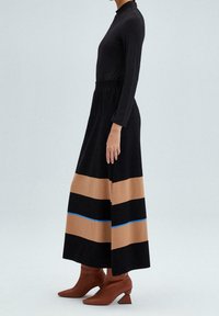 Vestido negro de manga larga con parte superior ajustada y falda acampanada con rayas horizontales marrones y negras, acentuado por una línea azul. Botas de tacón marrones.