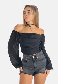 Zwarte top met blote schouders en opgeblazen, doorschijnende lange mouwen, gelaagde textuur, gecombineerd met hooggesneden zwarte denim shorts met distressed details.