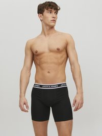 Schwarze Boxershorts mit einem weißen Bund, auf dem der Text "JACK & JONES" zu sehen ist. Das Material wirkt glatt und dehnbar und schmiegt sich eng an.