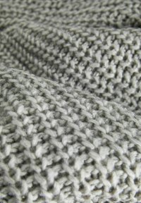 Knitted throw blanket in soft gray and white yarn, featuring textured patterns and a cozy, thick weave. Ideal for warmth and comfort.