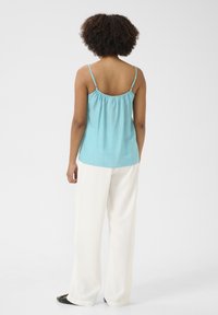 Šviesiai mėlynas, be rankovių palaidinė su reguliuojamomis špageti petnešėlėmis ir susiraukšlinta nugara, derinama su baltais plačiais kelnais ir juodais butais.