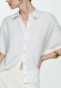 White linen shirt with short sleeves, a button-up front featuring light-colored buttons, and a loose, relaxed fit.