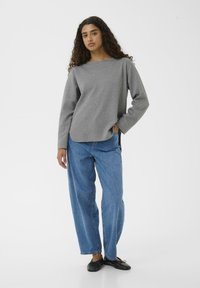 Maglietta grigia a maniche lunghe con scollatura rotonda abbinata a jeans blu a vita alta e scarpe nere basse. Taglio semplice e rilassato con spacchi laterali.