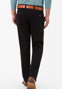 Chinos neri in cotone con taglio dritto, dotati di passanti per cintura, due tasche posteriori e una cintura in pelle color cuoio. Indossati con scarpe marroni.