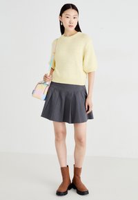 Suéter de malha amarelo claro, saia plissada cinza e botins castanhos com solas pretas. Apresenta uma pequena bolsa iridescente com uma alça.