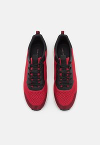 Pair of red and black knit athletic shoes with black laces, pull tabs on heels, and white soles shown from above on white background.