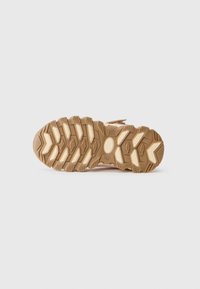 Suela de zapatilla de trail con un diseño de goma rugosa y con patrón. Presenta una mezcla de colores beige claro y marrón claro, proporcionando tracción y durabilidad.