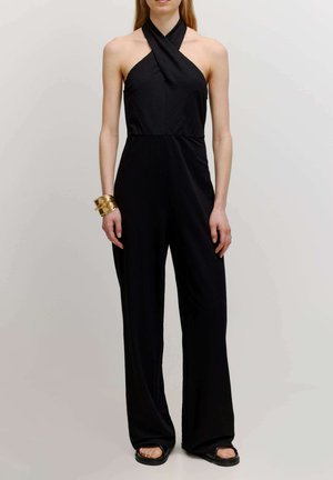 Zwart jumpsuit met halternek ontwerp. Materiaal lijkt glad. Heeft brede pijpen en een aansluitend lijfje. Gouden armband als accent.