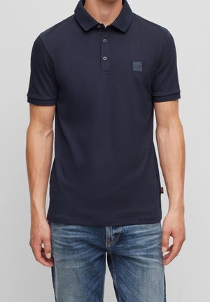 Polo bleu marine à manches courtes, patte de boutonnage à trois boutons et patch logo carré sur la poitrine gauche. Tissu lisse avec une coupe ajustée.