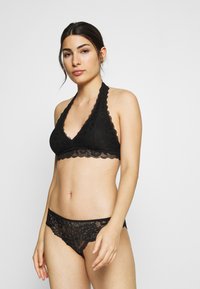 Schwarzes Spitzen-Bralette und passende Unterhose mit gewellten Kanten und floralem Muster. Weiches, dehnbares Material mit einem Halterneck-Design.