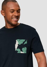 Zwarte T-shirt met een textuurfinish, voorzien van een groen-wit bladpatroon op de linkerkant van de borst.