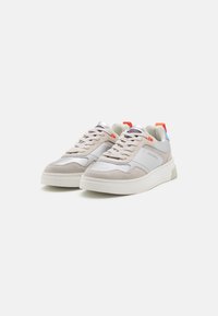 Des baskets gris clair avec un mélange de daim et de matériaux synthétiques. Bout arrondi, semelle blanche et accents colorés sur le talon et la languette.