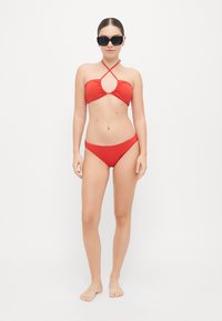 Bikini rouge avec un haut à nouer sur le devant, col halter, et un bas assorti taille basse. Texture lisse, design minimaliste, et sans motifs visibles.
