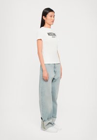 White cotton t-shirt with black "MOSCHINO JEANS" print, paired with light blue relaxed-fit denim jeans and white sneakers.