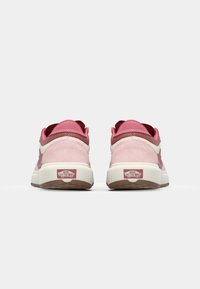 Sneakers roz din suede, cu accente albe, având o talpă căptușită, spate texturat și logo-ul Vans pe călcâi. Suprafață netedă și formă rotunjită.