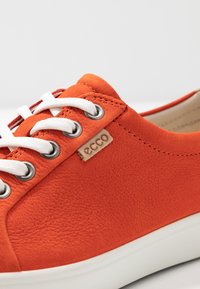 Zapatillas de cuero naranja con cordones blancos, ojetes de metal y una pequeña etiqueta con el logo de ECCO en el costado. Acabado texturizado y diseño de puntera redondeada.