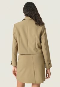 Beige dubbelknäppt kavaj med en kortad design och långa ärmar, kombinerad med en matchande figurnära kjol, som har rena linjer och minimal detaljering.