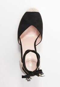 Espadrille en suède noir avec un orteil en crochet beige, une sangle élastique à la cheville et un détail de nœud noir décoratif. Doublure intérieure lisse.