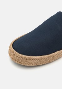 Botte en toile marine à enfiler avec une semelle en jute tressée, présentant une texture tressée sur le bord. Bout arrondi et surface supérieure lisse.