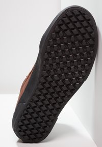 Hnědá teniska s texturovanou černou gumovou podešví s diamantovým vzorem. Vrchní materiál vypadá jako semiš s detailem prošívání.