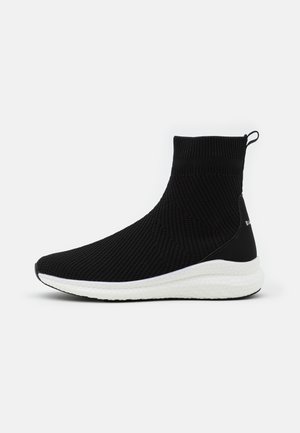 Black knitted ankle-height sneaker with a white sole, featuring a textured pattern, pull tab, and smooth black accents on the heel.