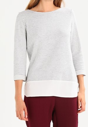 Maglietta a maniche lunghe con un motivo a righe bianco e grigio, con un orlo bianco tinta unita e una texture liscia. Abbinata a pantaloni bordeaux.