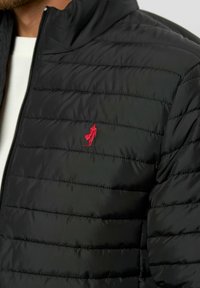 Crni puffer jakna s horizontalnim prešanim dijelovima, s crvenim izvezenim logotipom na lijevoj strani prsnog dijela i zatvaračem sprijeda.