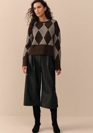 Hnědo-bílý svetr se vzorem s geometrickým designem, kombinovaný s černými koženými culottes a černými vysokými podpatky.