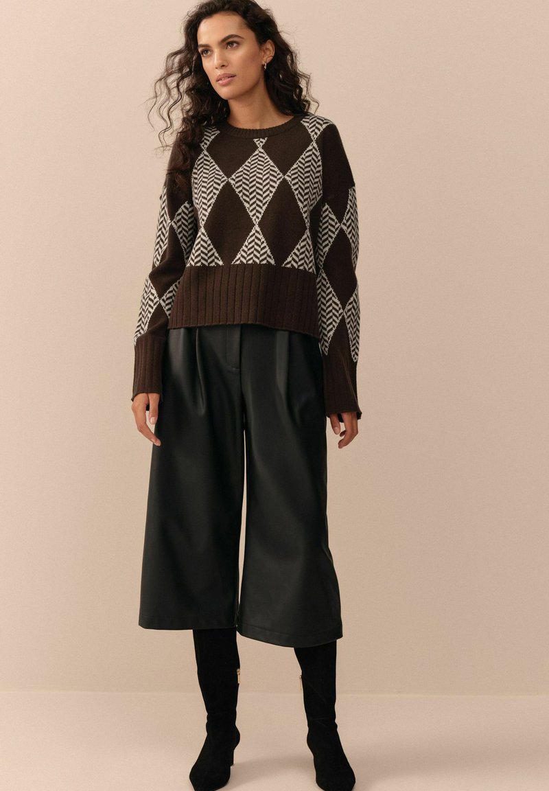 Suéter de diseño geométrico en tonos marrón y blanco, combinado con culottes de cuero negro y botas de tacón alto negras.
