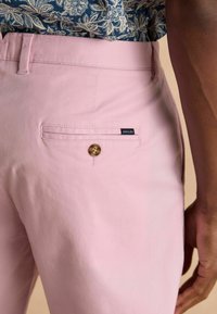 Helle rosa Hose aus Baumwolle, mit einer Gesäßtasche mit Knopfverschluss und einem Etikett mit der Aufschrift "JOULES" an der Tasche.