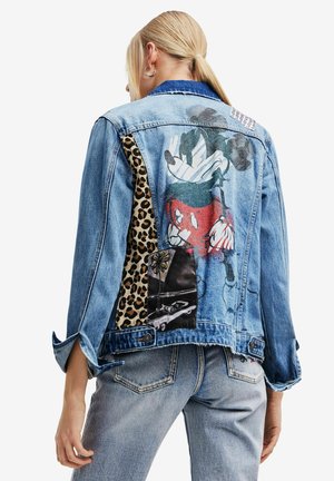 Mujer con chaqueta de mezclilla azul claro con gráfico de Mickey Mouse, parche de estampado de leopardo y parche con foto de coche en la espalda, combinada con jeans a juego.