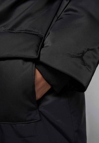 Giacca a vento nera con una finitura liscia e lucida. Presenta una tasca laterale, polsini a coste e un logo Jumpman ricamato sulla manica.
