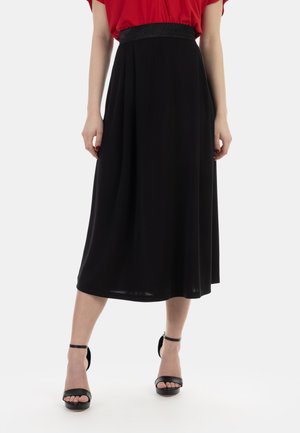 Gonna nera midi con un elastico lucido in vita, caratterizzata da una texture liscia e una silhouette fluida. Abbinata a décolleté nere con cinturino alla caviglia.