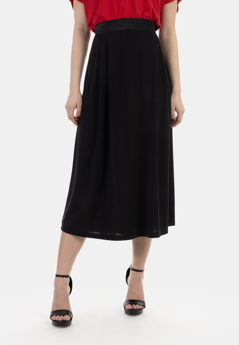 Gonna nera midi con un elastico lucido in vita, caratterizzata da una texture liscia e una silhouette fluida. Abbinata a décolleté nere con cinturino alla caviglia.