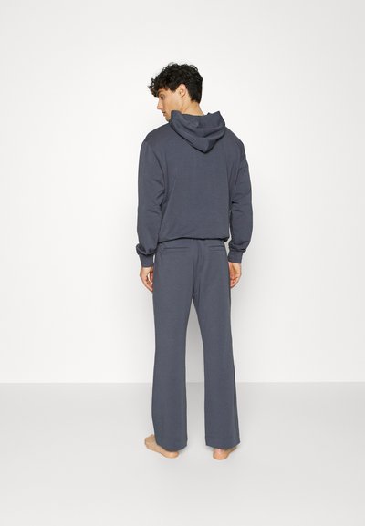 Sweatshirt cinza e calças combinando feitas de tecido macio. O hoodie apresenta um cordão e um bolso canguru; as calças são largas com um corte reto.