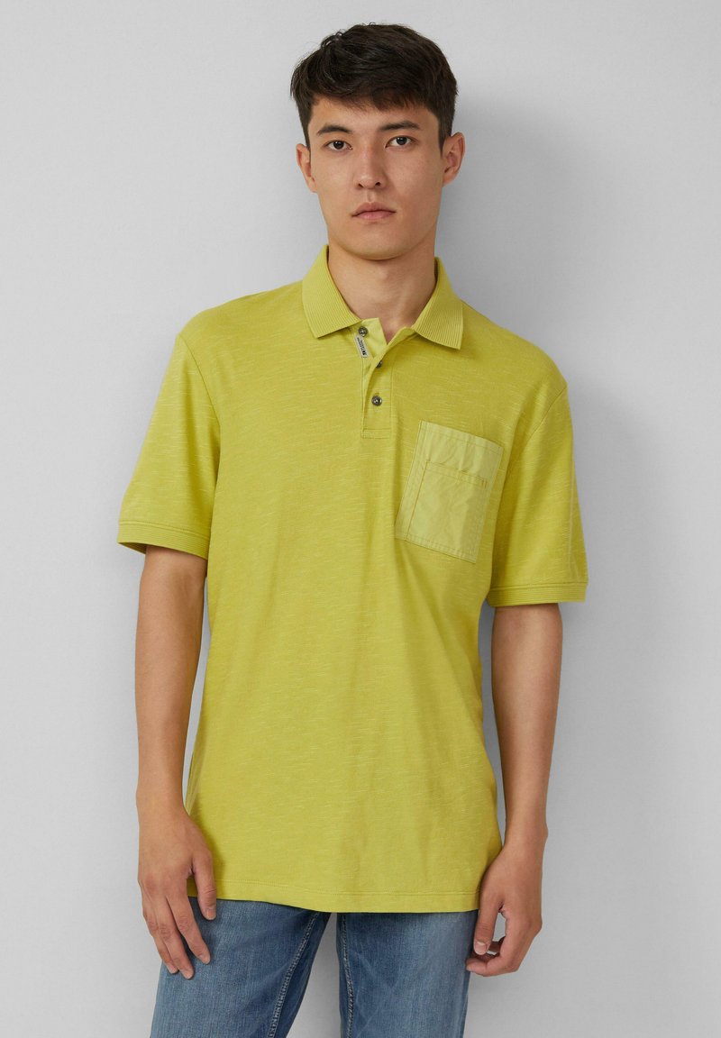 Jasnozielona koszulka polo z kołnierzykiem, krótkimi rękawami i kieszonką na piersi. Teksturowana tkanina, zapięcie na guziki i luźny krój.