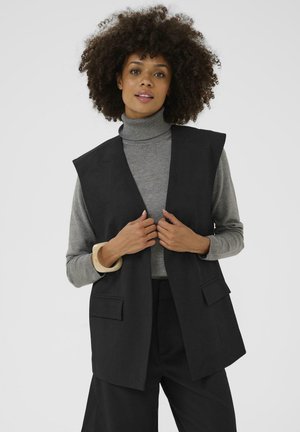 Black sleeveless vest with a straight, tailored design. Features side pockets and is worn over a gray turtleneck sweater. Smooth texture.
