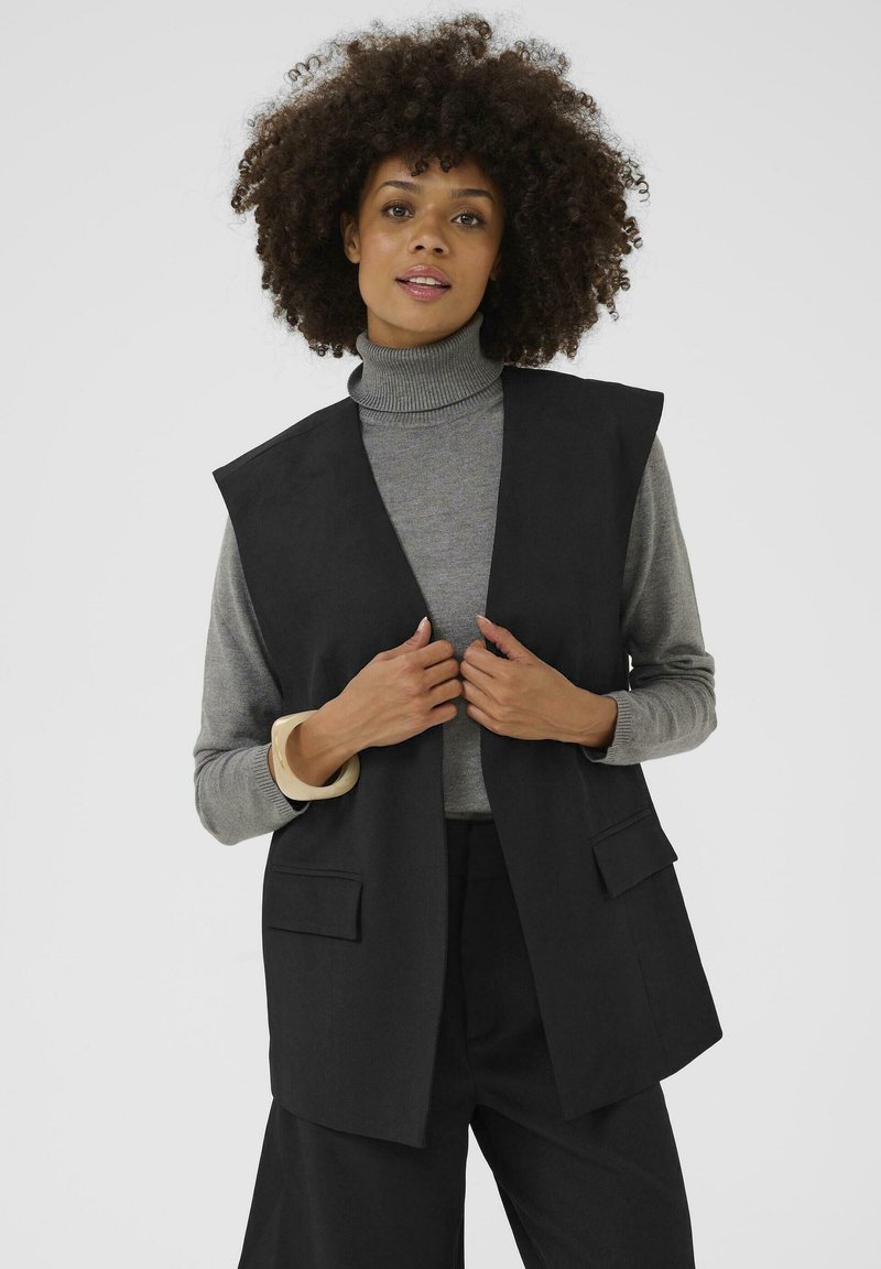 Black sleeveless vest with a straight, tailored design. Features side pockets and is worn over a gray turtleneck sweater. Smooth texture.