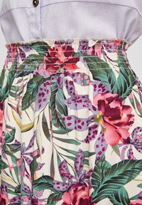 Gros plan d’une jupe fleurie avec des motifs colorés de fleurs tropicales roses, violettes et vertes, portée avec un haut violet clair.