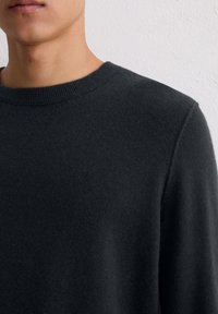 Ciemnoszary sweter wykonany z miękkiego materiału, z klasycznym okrąg�łym dekoltem i ściągaczem. Tekstura wygląda na gładką i drobno dziewiarską.