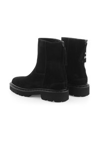 Zwarte suède enkellaarsjes met een grove zool, ritssluitingen aan de zijkant en kwastaccenten. Heeft een gladde textuur en contrasterende stiksel details.