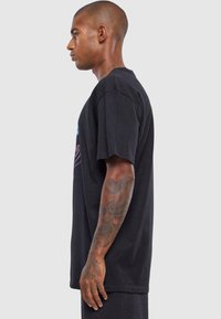 Sort bomulds t-shirt med korte ærmer, afslappet pasform og farverigt grafisk tryk på forsiden. Har en rund halsudskæring og en glat tekstur.