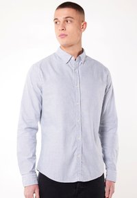 Chemise à manches longues rayée bleu et blanche avec un col à bouton, dotée de petits boutons et d'un ourlet arrondi. Fabriquée en tissu léger.